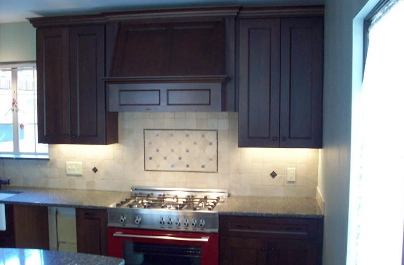 Example of an eat-in kitchen design in Cleveland with recessed-panel cabinets, dark wood cabinets, granite countertops, beige backsplash, ceramic backsplash, stainless steel appliances and an island
