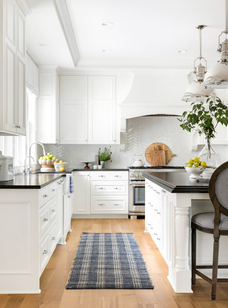 Design ideas for a large beach style l-shaped eat-in kitchen in Minneapolis with a farmhouse sink, beaded inset cabinets, white cabinets, quartz benchtops, white splashback, mosaic tile splashback, stainless steel appliances, light hardwood floors, with island, brown floor and white benchtop.