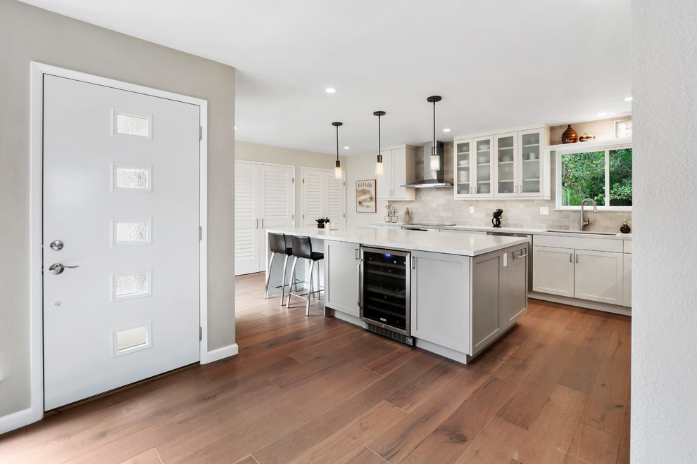 Mid-sized transitional l-shaped medium tone wood floor and brown floor kitchen pantry photo with an undermount sink, shaker cabinets, white cabinets, quartz countertops, beige backsplash, subway tile backsplash, stainless steel appliances, an island and beige countertops
