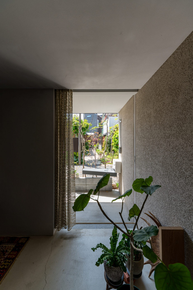 Kleiner Eingang mit Korridor, grauer Wandfarbe, Betonboden, Schiebetür, hellbrauner Holzhaustür und grauem Boden in Tokio