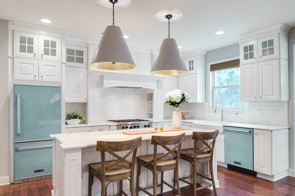 This is an example of a transitional l-shaped kitchen in Philadelphia with a farmhouse sink, raised-panel cabinets, white cabinets, white splashback, subway tile splashback, coloured appliances, medium hardwood floors, with island and brown floor.