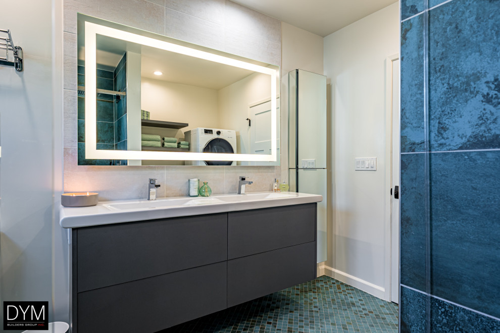 This is an example of a large contemporary master bathroom in Los Angeles with flat-panel cabinets, grey cabinets, an alcove shower, a one-piece toilet, white tile, marble, white walls, mosaic tile floors, a drop-in sink, solid surface benchtops, blue floor, a hinged shower door, white benchtops, a laundry, a double vanity, a built-in vanity, wallpaper and wallpaper.