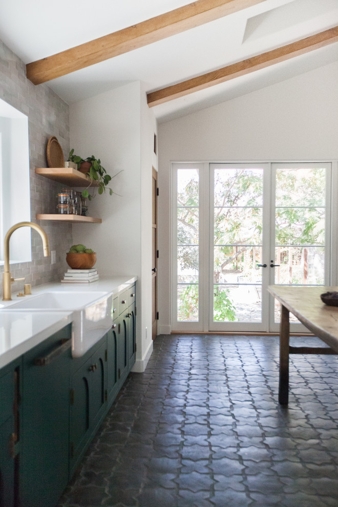 Design ideas for a mid-sized mediterranean open plan kitchen in Los Angeles with a farmhouse sink, flat-panel cabinets, green cabinets, quartz benchtops, white splashback, subway tile splashback, panelled appliances, ceramic floors, no island, black floor and white benchtop.
