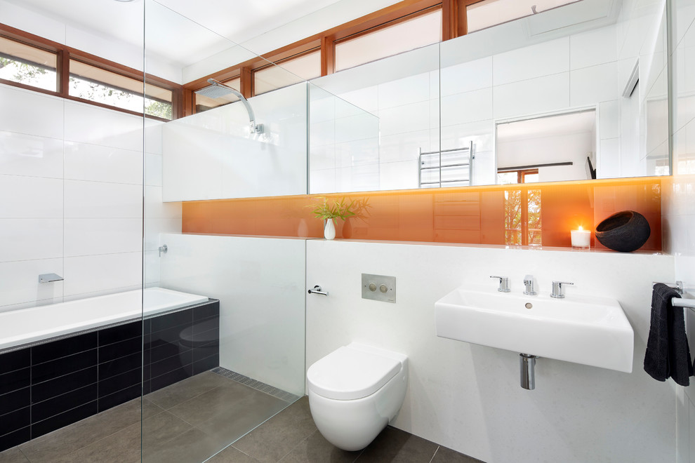 Design ideas for a mid-sized modern master bathroom in Melbourne with a wall-mount sink, a drop-in tub, a curbless shower, a wall-mount toilet, black tile, ceramic tile, white walls, ceramic floors, grey floor and a niche.