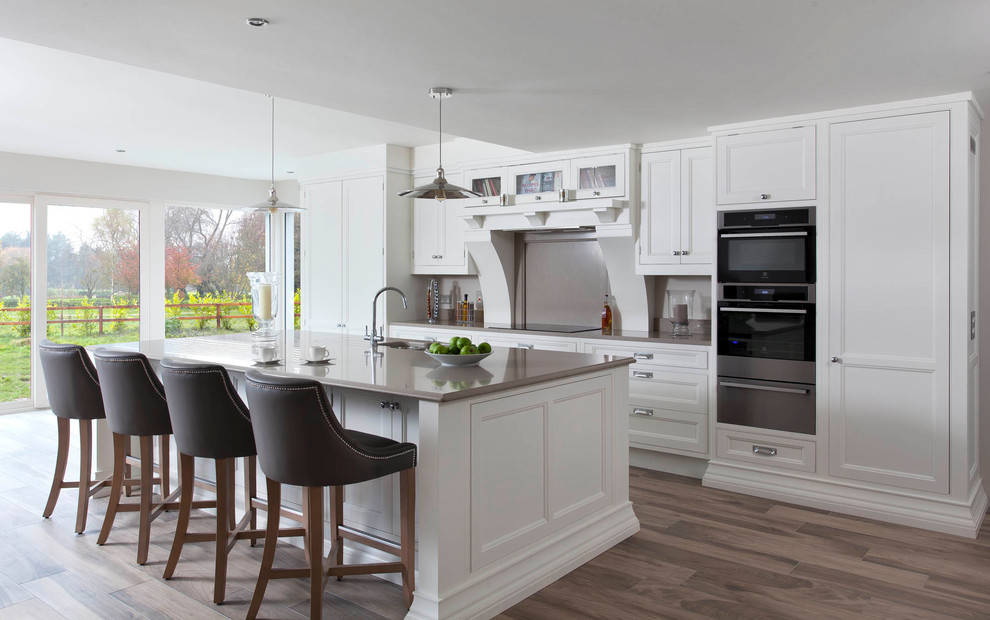 Photo of a large traditional single-wall open plan kitchen in Other with an integrated sink, beaded inset cabinets, white cabinets, quartzite benchtops, brown splashback, stone slab splashback, stainless steel appliances, medium hardwood floors, with island and brown floor.