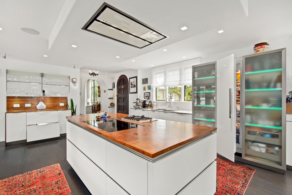 This is an example of a large contemporary l-shaped kitchen pantry in Other with flat-panel cabinets, white cabinets, wood benchtops, white splashback, white appliances, with island, brown floor and brown benchtop.