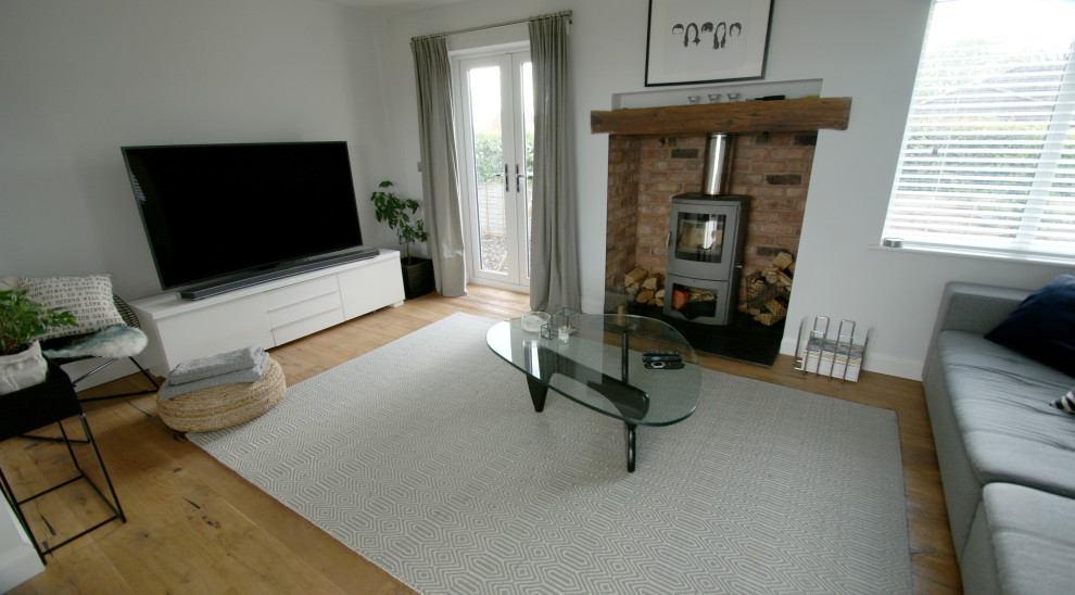 Mittelgroßes, Offenes Skandinavisches Wohnzimmer mit braunem Holzboden, Kaminofen, Kaminumrandung aus Backstein und freistehendem TV in West Midlands