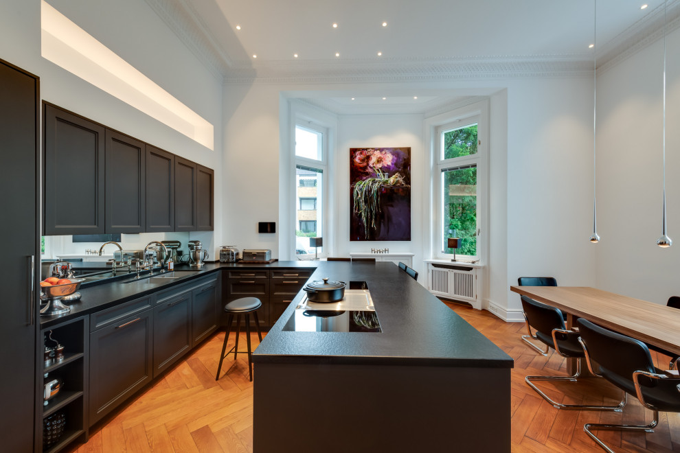 Expansive contemporary u-shaped open plan kitchen in Hamburg with a double-bowl sink, beaded inset cabinets, black cabinets, laminate benchtops, white splashback, mirror splashback, black appliances, painted wood floors, a peninsula, brown floor, black benchtop and vaulted.