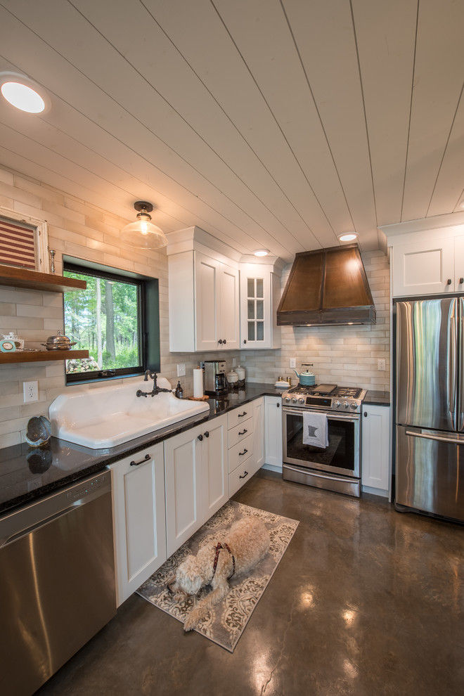 Example of a mid-sized mountain style l-shaped concrete floor and gray floor open concept kitchen design in Minneapolis with a drop-in sink, shaker cabinets, white cabinets, solid surface countertops, beige backsplash, subway tile backsplash, stainless steel appliances, an island and black countertops