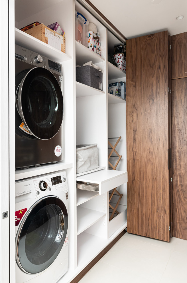 Inspiration for a small contemporary galley laundry cupboard in London with flat-panel cabinets, dark wood cabinets, brown walls, ceramic floors, a stacked washer and dryer, beige floor and wood walls.