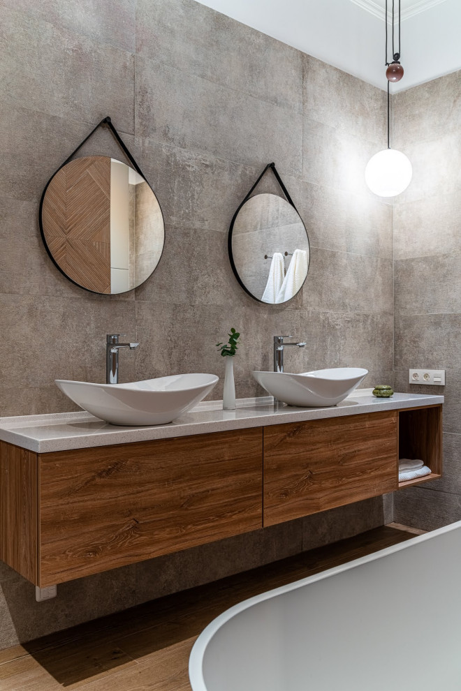 This is an example of a mid-sized scandinavian master bathroom in Saint Petersburg with flat-panel cabinets, brown cabinets, a freestanding tub, a shower/bathtub combo, a wall-mount toilet, gray tile, porcelain tile, brown walls, ceramic floors, a vessel sink, solid surface benchtops, brown floor, an open shower, grey benchtops, an enclosed toilet, a double vanity, a floating vanity, recessed and decorative wall panelling.