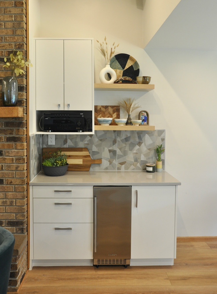 Photo of a small transitional single-wall home bar in Minneapolis with no sink, flat-panel cabinets, white cabinets, quartz benchtops, grey splashback, cement tile splashback, medium hardwood floors, brown floor and grey benchtop.