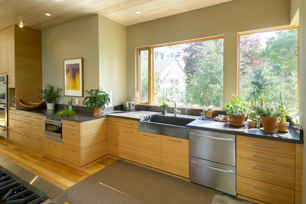Photo of a large contemporary open plan kitchen in Boston with a farmhouse sink, flat-panel cabinets, beige cabinets, concrete benchtops, stainless steel appliances, bamboo floors and with island.