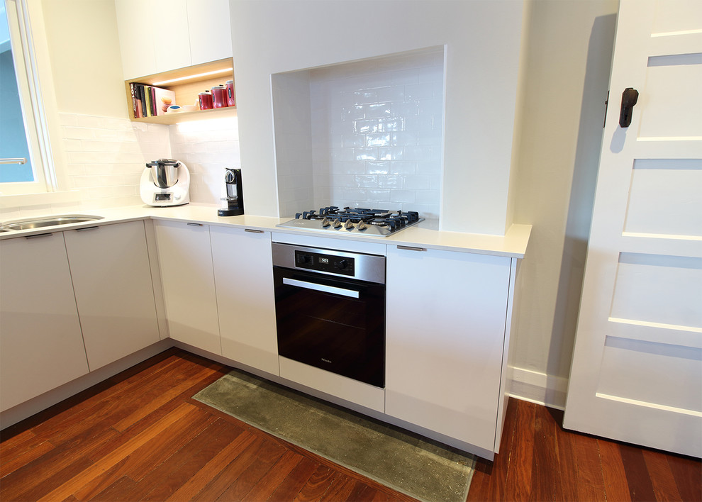 Traditional u-shaped kitchen in Perth with white cabinets, white splashback, a peninsula, brown floor and white benchtop.