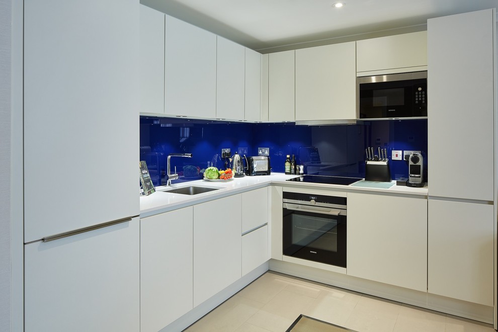 Inspiration for a contemporary kitchen in London with an undermount sink, flat-panel cabinets, white cabinets, blue splashback, glass sheet splashback, stainless steel appliances, beige floor and white benchtop.