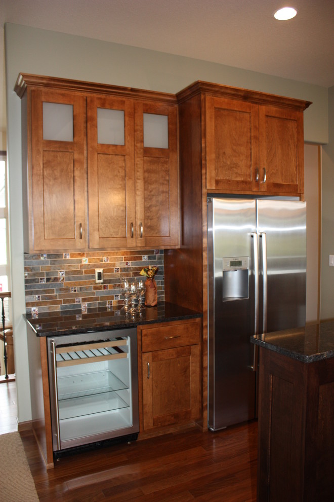 Example of a mid-sized transitional l-shaped medium tone wood floor home design design with an undermount sink, recessed-panel cabinets, medium tone wood cabinets, granite countertops, multicolored backsplash, mosaic tile backsplash, stainless steel appliances and an island