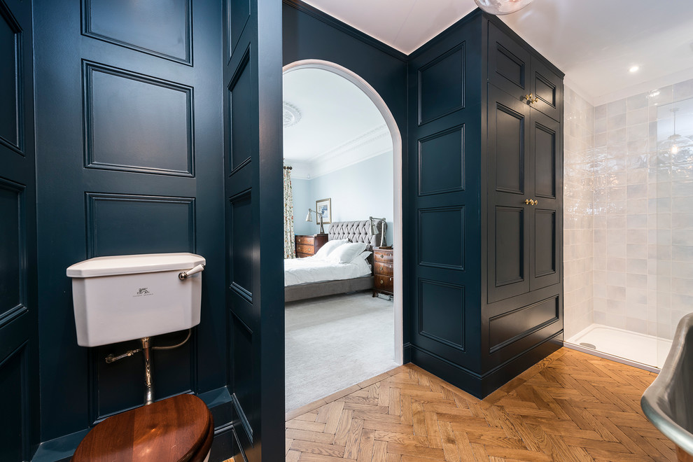 Inspiration for a large transitional master bathroom in London with a wall-mount sink, a freestanding tub, a shower/bathtub combo, a one-piece toilet, blue walls and light hardwood floors.