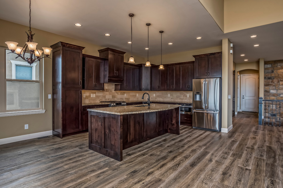 This is an example of a large mediterranean l-shaped open plan kitchen in Denver with an undermount sink, dark wood cabinets, granite benchtops, beige splashback, stainless steel appliances, medium hardwood floors and with island.