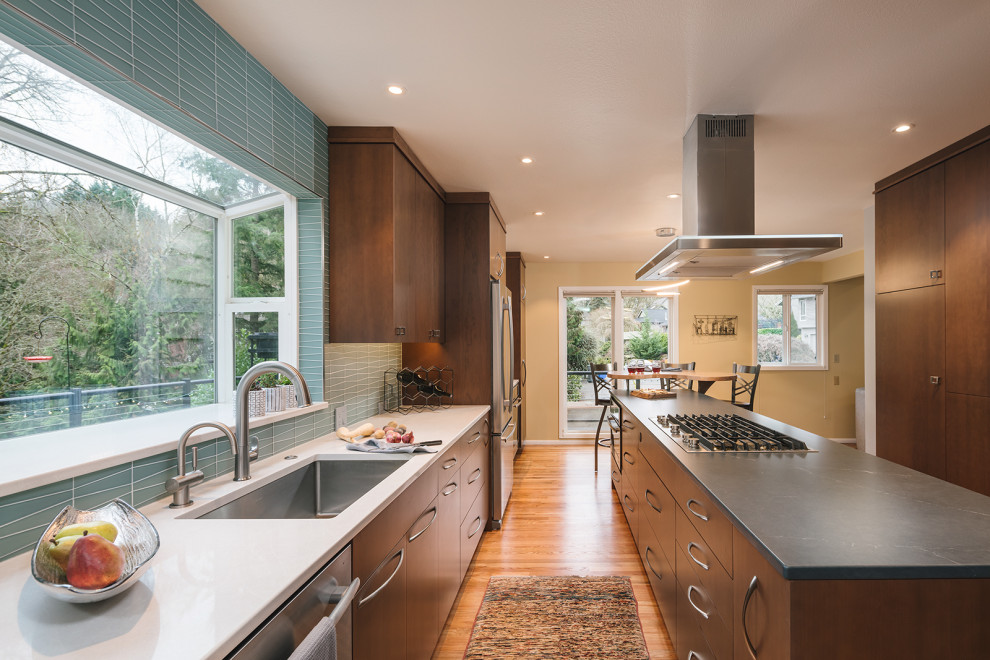 Inredning av ett modernt mellanstort flerfärgad flerfärgat kök, med en undermonterad diskho, släta luckor, skåp i mörkt trä, bänkskiva i kvarts, blått stänkskydd, stänkskydd i glaskakel, rostfria vitvaror, mellanmörkt trägolv, en köksö och brunt golv
