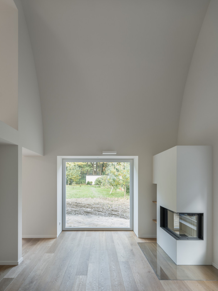 Minimalist loft-style medium tone wood floor, brown floor and vaulted ceiling family room photo in Hamburg with white walls, a corner fireplace and a plaster fireplace