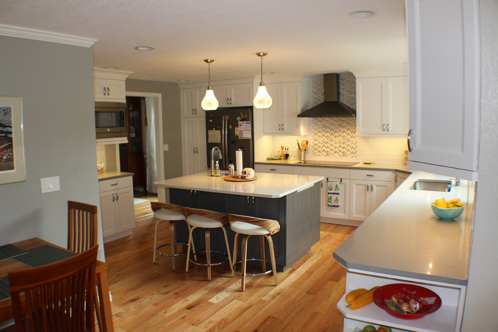 Inspiration for a mid-sized transitional l-shaped medium tone wood floor and brown floor eat-in kitchen remodel with an undermount sink, shaker cabinets, white cabinets, quartz countertops, white backsplash, stainless steel appliances, an island and gray countertops