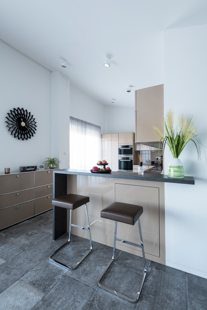 Design ideas for a small contemporary l-shaped open plan kitchen in Nuremberg with flat-panel cabinets, brown cabinets, black appliances, a peninsula, grey floor and black benchtop.