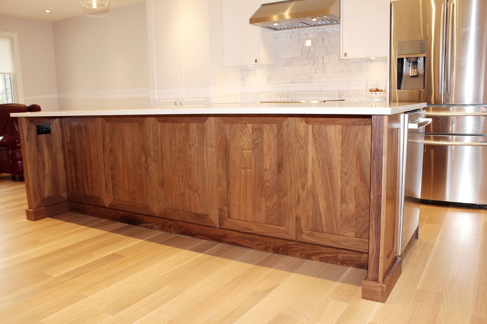 Large transitional l-shaped light wood floor eat-in kitchen photo with an undermount sink, shaker cabinets, white cabinets, quartz countertops, white backsplash, ceramic backsplash, stainless steel appliances and an island