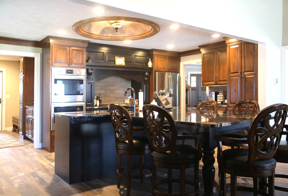 Eat-in kitchen - mid-sized transitional l-shaped porcelain tile eat-in kitchen idea with an undermount sink, raised-panel cabinets, medium tone wood cabinets, granite countertops, beige backsplash, porcelain backsplash, stainless steel appliances and an island