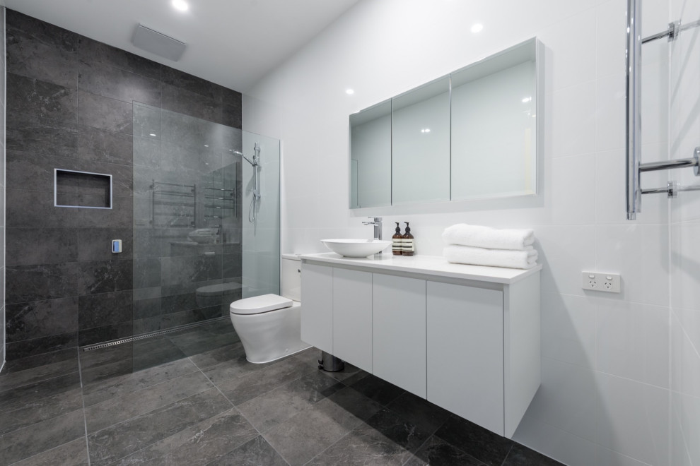 Inspiration for a mid-sized modern master bathroom in Other with raised-panel cabinets, white cabinets, an open shower, a one-piece toilet, gray tile, ceramic tile, grey walls, ceramic floors, an integrated sink, engineered quartz benchtops, grey floor, a hinged shower door, white benchtops, a single vanity and a floating vanity.