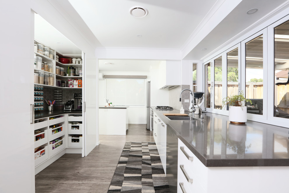 Inspiration for a mid-sized modern galley open plan kitchen in Melbourne with flat-panel cabinets, white cabinets, quartz benchtops, with island, a double-bowl sink, mosaic tile splashback, stainless steel appliances, vinyl floors and grey benchtop.