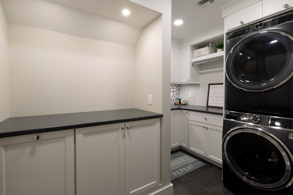 Example of a mid-sized transitional l-shaped dedicated laundry room design in New York with an undermount sink, shaker cabinets, white cabinets, quartz countertops, multicolored backsplash, mosaic tile backsplash, beige walls, a stacked washer/dryer and black countertops