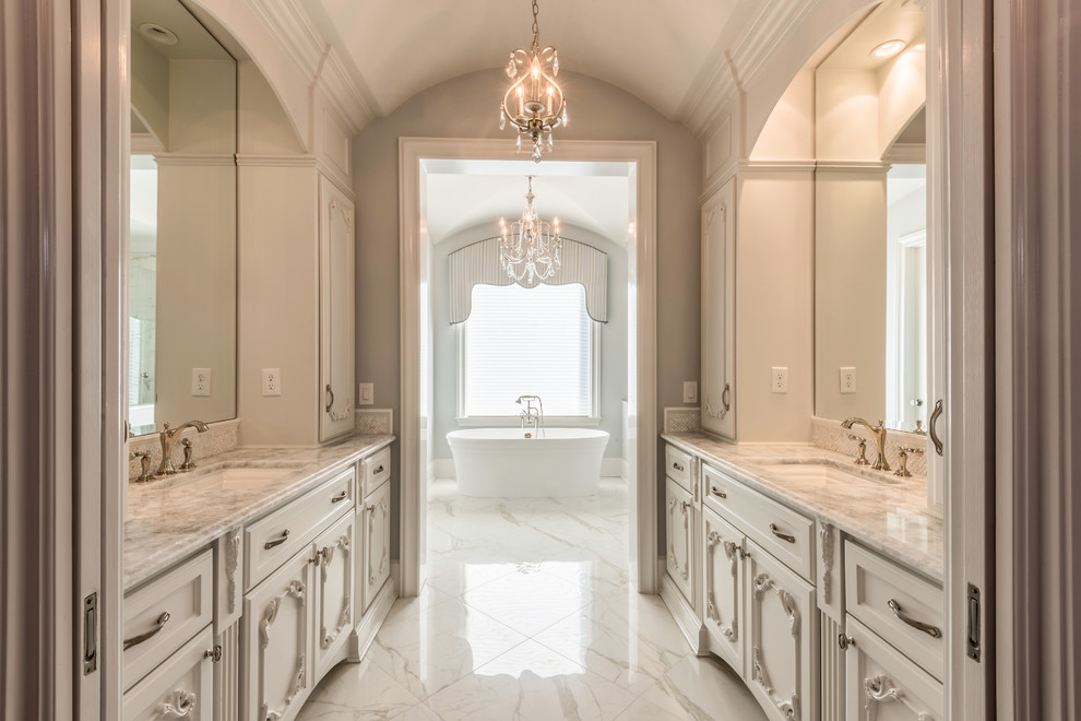 This is an example of a large traditional master bathroom in Houston with white cabinets, a freestanding tub, grey walls, an undermount sink, white floor, ceramic floors, a corner shower, quartzite benchtops, a hinged shower door, white benchtops and recessed-panel cabinets.