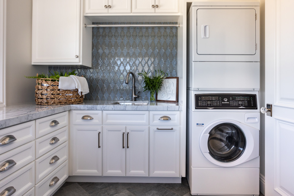 This is an example of a small beach style u-shaped utility room in Sacramento with an undermount sink, recessed-panel cabinets, white cabinets, quartzite benchtops, blue splashback, porcelain splashback, grey walls, ceramic floors, a stacked washer and dryer, grey floor, grey benchtop and wood.