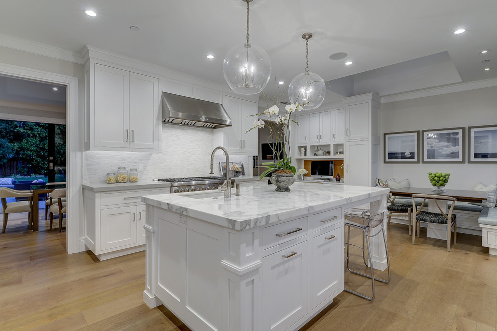 Photo of a transitional galley kitchen in San Francisco with an undermount sink, shaker cabinets, white cabinets, white splashback, mosaic tile splashback, medium hardwood floors, with island and brown floor.