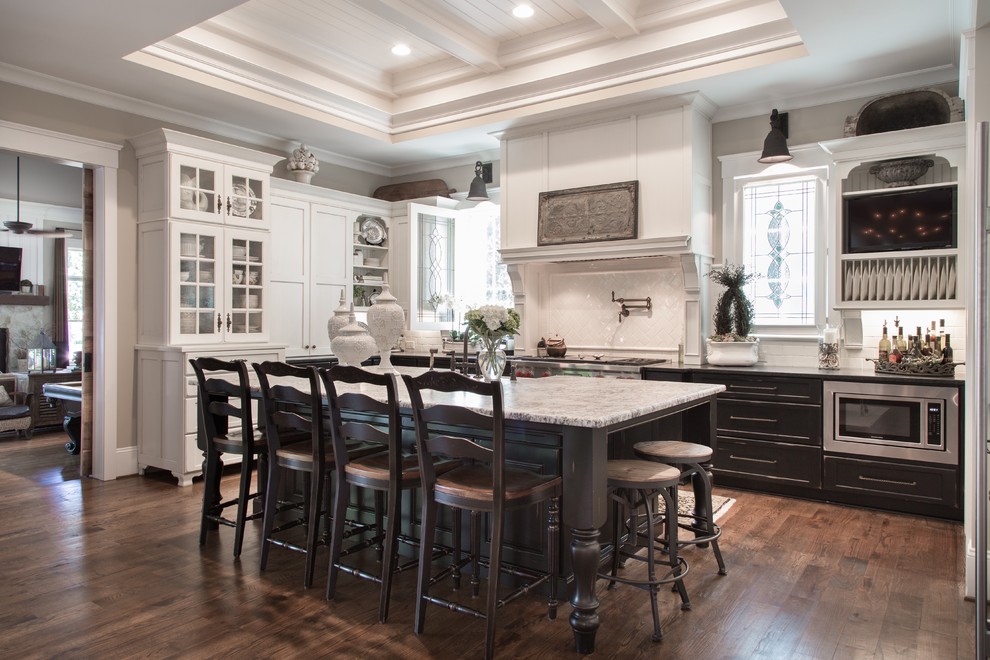 Design ideas for a traditional kitchen in Charlotte with a farmhouse sink, distressed cabinets, granite benchtops, white splashback, subway tile splashback, stainless steel appliances, light hardwood floors and with island.
