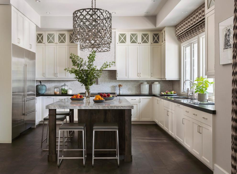 This is an example of a mediterranean u-shaped kitchen in Los Angeles with an undermount sink, shaker cabinets, white cabinets, grey splashback, stainless steel appliances, with island, brown floor and black benchtop.