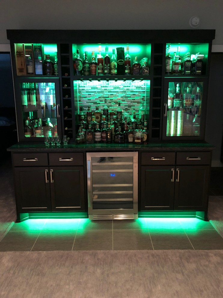 This is an example of a mid-sized traditional single-wall home bar in Other with no sink, dark wood cabinets, granite benchtops, multi-coloured splashback, glass sheet splashback, vinyl floors, multi-coloured floor and multi-coloured benchtop.