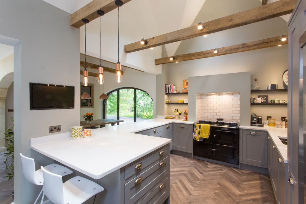 Photo of a large classic l-shaped kitchen/diner in Gloucestershire with a submerged sink, raised-panel cabinets, grey cabinets, composite countertops, white splashback, black appliances, medium hardwood flooring, a breakfast bar and a feature wall.