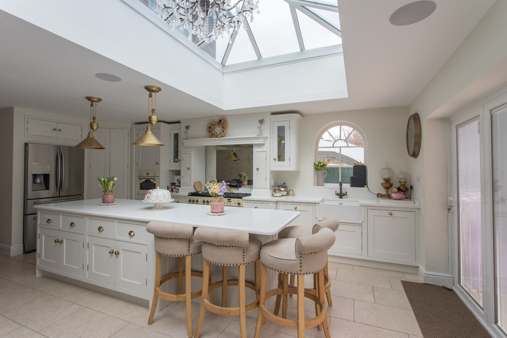 This is an example of a large traditional l-shaped eat-in kitchen in Hertfordshire with a single-bowl sink, shaker cabinets, yellow cabinets, soapstone benchtops, metallic splashback, mirror splashback, stainless steel appliances, porcelain floors, with island, beige floor and white benchtop.