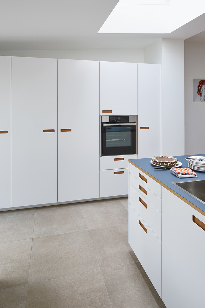 Inspiration for an expansive modern galley open plan kitchen in Bonn with a double-bowl sink, flat-panel cabinets, white cabinets, wood worktops, stainless steel appliances, ceramic flooring and a breakfast bar.