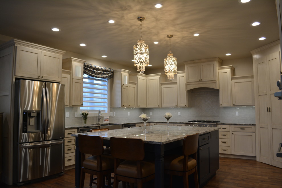 Example of a mid-sized transitional l-shaped medium tone wood floor eat-in kitchen design with a farmhouse sink, shaker cabinets, white cabinets, granite countertops, white backsplash, subway tile backsplash, stainless steel appliances and an island