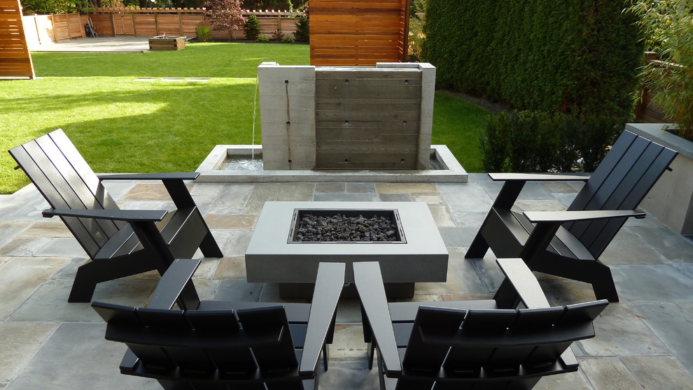 This is an example of a mid-sized arts and crafts backyard patio in Vancouver with a fire feature, natural stone pavers and a roof extension.