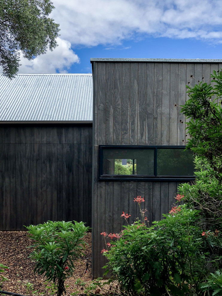 Photo of a small country one-storey black house exterior in Adelaide with wood siding, a gable roof and a metal roof.