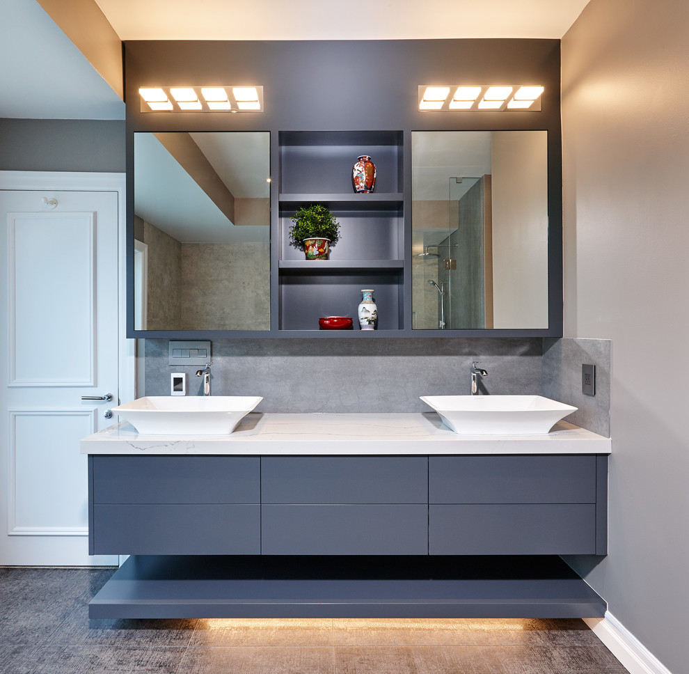 Photo of a large contemporary master bathroom in Toronto with flat-panel cabinets, grey cabinets, a corner shower, a two-piece toilet, gray tile, stone slab, grey walls, medium hardwood floors, a vessel sink, quartzite benchtops, brown floor, a hinged shower door and white benchtops.