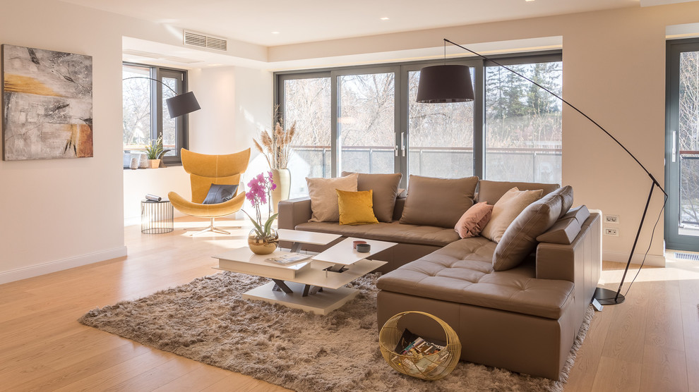 This is an example of a mid-sized contemporary formal open concept living room in Manchester with light hardwood floors, no fireplace and beige walls.