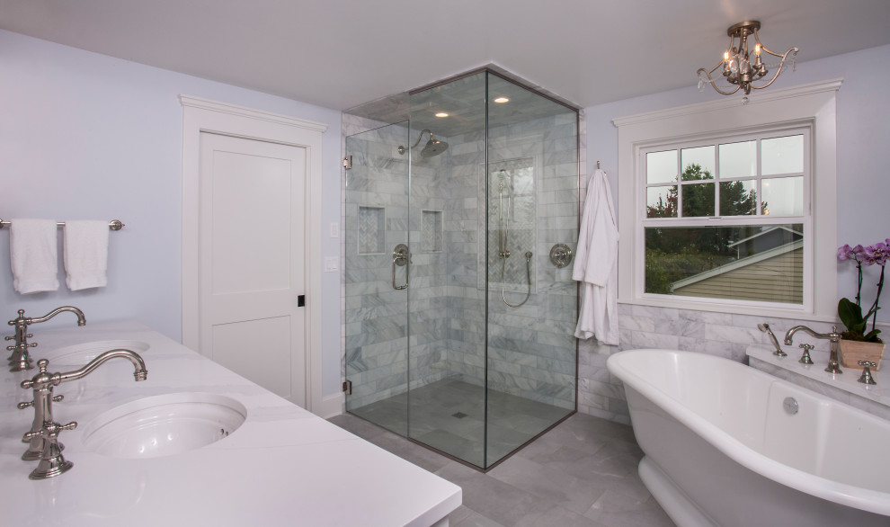 На фото: большая главная ванная комната в классическом стиле с фасадами в стиле шейкер, белыми фасадами, отдельно стоящей ванной, душем без бортиков, раздельным унитазом, белой плиткой, мраморной плиткой, синими стенами, полом из керамогранита, врезной раковиной, столешницей из искусственного кварца, серым полом, душем с распашными дверями, белой столешницей, нишей, тумбой под две раковины, напольной тумбой и панелями на стенах