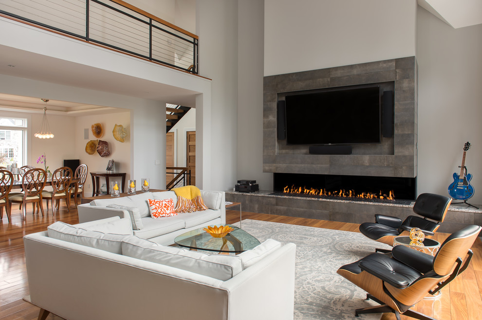 Large contemporary open concept family room in Boston with grey walls, light hardwood floors, a ribbon fireplace, a tile fireplace surround, a concealed tv and beige floor.