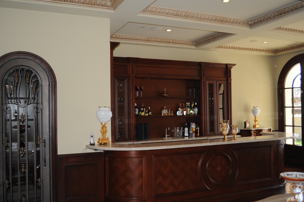Photo of a mid-sized single-wall seated home bar in Orange County with an undermount sink, recessed-panel cabinets, dark wood cabinets, limestone benchtops, limestone floors and beige floor.