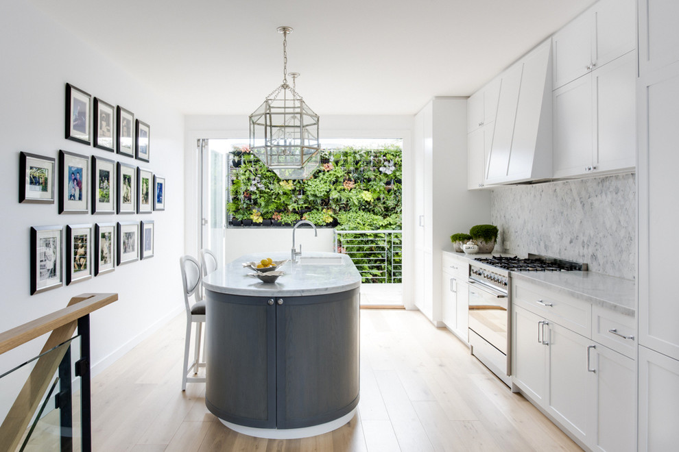 Inspiration for a transitional kitchen in Melbourne with an undermount sink, shaker cabinets, white cabinets, white splashback, stainless steel appliances, light hardwood floors and with island.