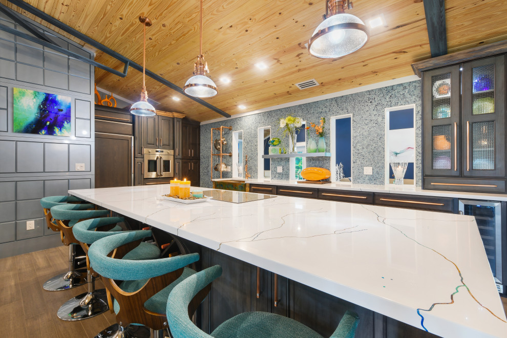 Expansive eclectic l-shaped eat-in kitchen in Miami with a farmhouse sink, raised-panel cabinets, brown cabinets, solid surface benchtops, blue splashback, glass sheet splashback, stainless steel appliances, bamboo floors, with island, brown floor and white benchtop.